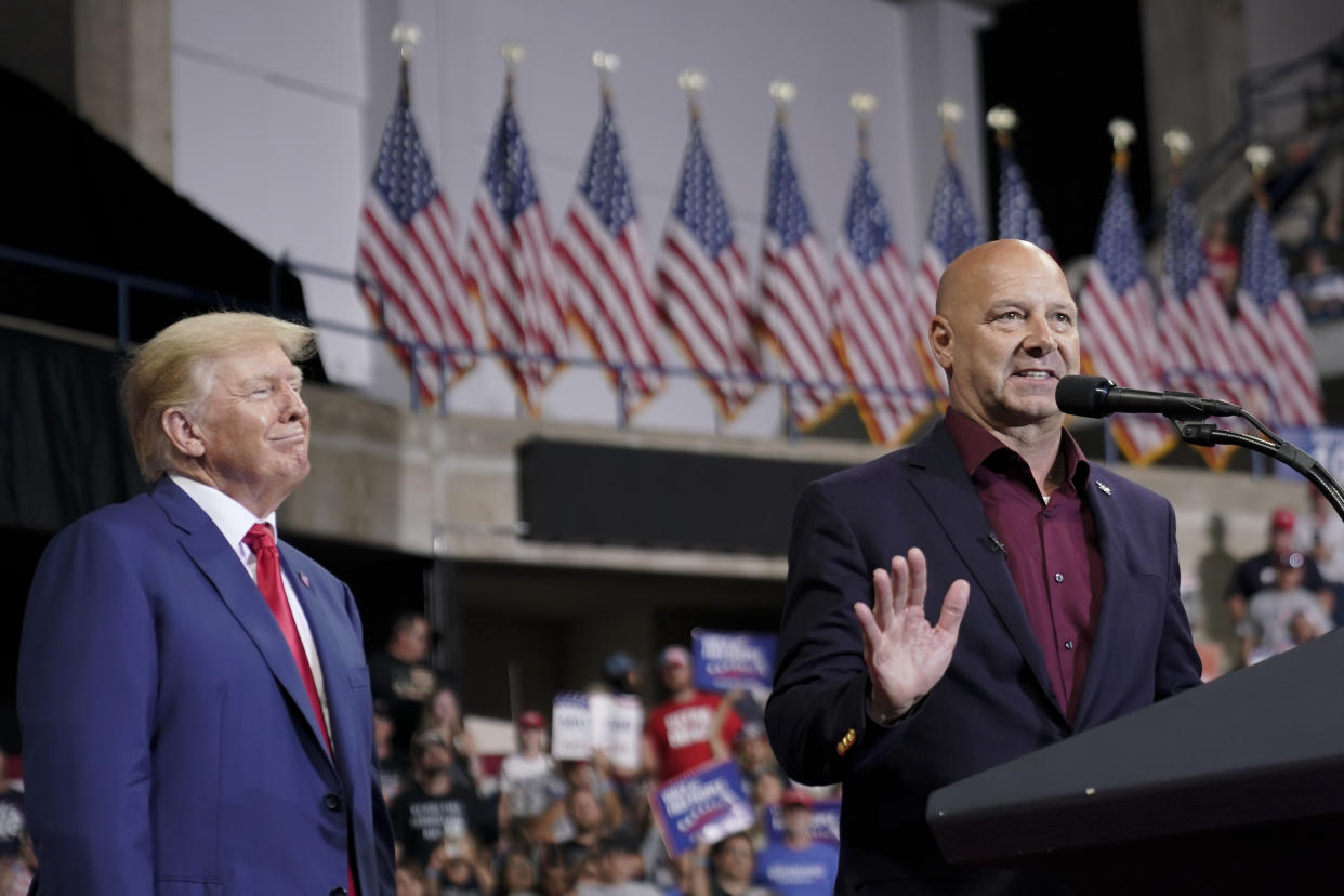 Former President Donald Trump stands to the side of Doug Mastriano, who is standing at a podium.