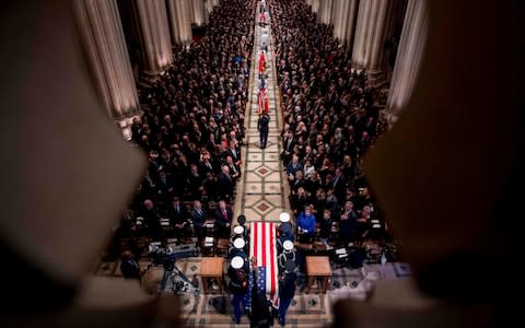 The flag-draped casket of former US President George H W Bush arrives carried by a military honor guard during a State Funeral at the National Cathedral  - Credit: ANDREW HARNIK/AFP