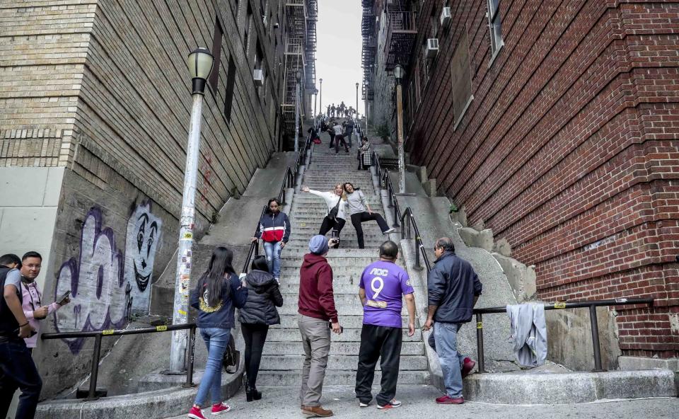 People pose on the steps between two apartment buildings, Monday Oct. 28, 2019, in the Bronx borough of New York. The stairs have become a tourist attraction in recent weeks since the release of the movie “Joker.” In the movie, lead actor Joaquin Phoenix dances as he goes down the steps, wearing a bright red suit and clown makeup. (AP Photo/Bebeto Matthews)