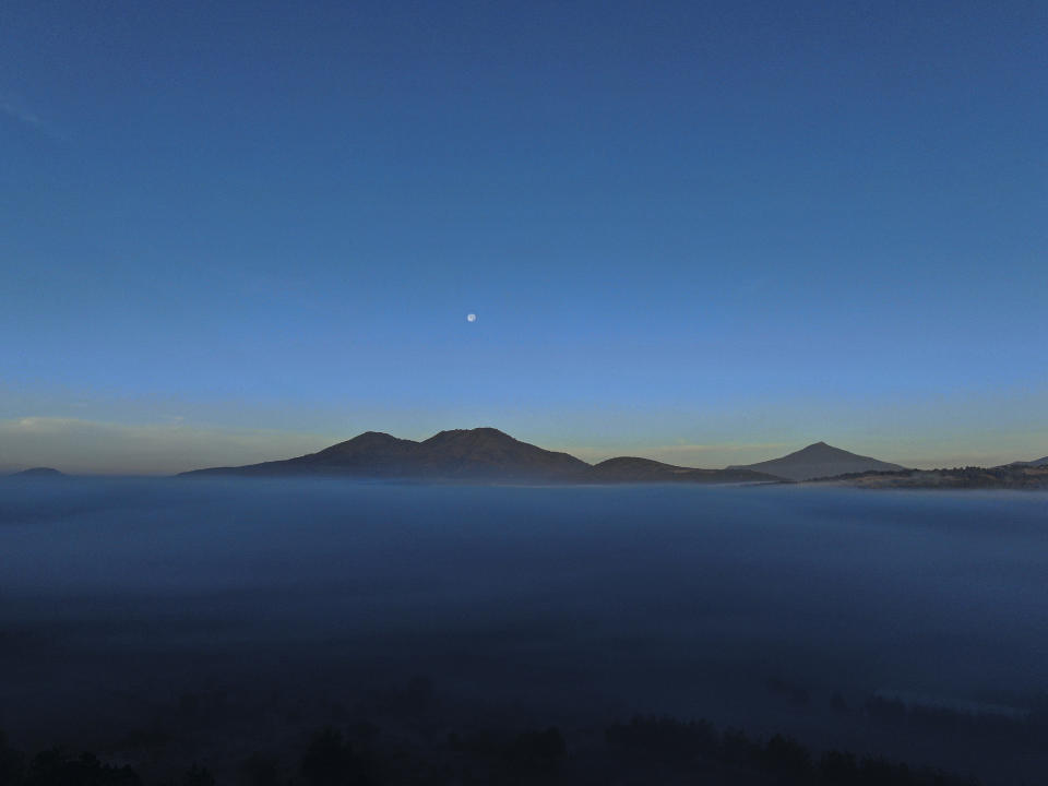 The moon rises over the pine-covered mountains surrounding the Indigenous township of Cheran, Michoacan state, Mexico, Wednesday, Jan. 19, 2022. Avocados have been nothing short of a miracle crop for thousands of small farmers in Michoacan; with a few acres of well-tended avocado trees, small landholders can send their kids to college or buy a pickup truck, something no other crop allows them to do. But because of the immense amount of water they need, the expansion of avocados has come by moving into humid pine forests. (AP Photo/Fernando Llano)