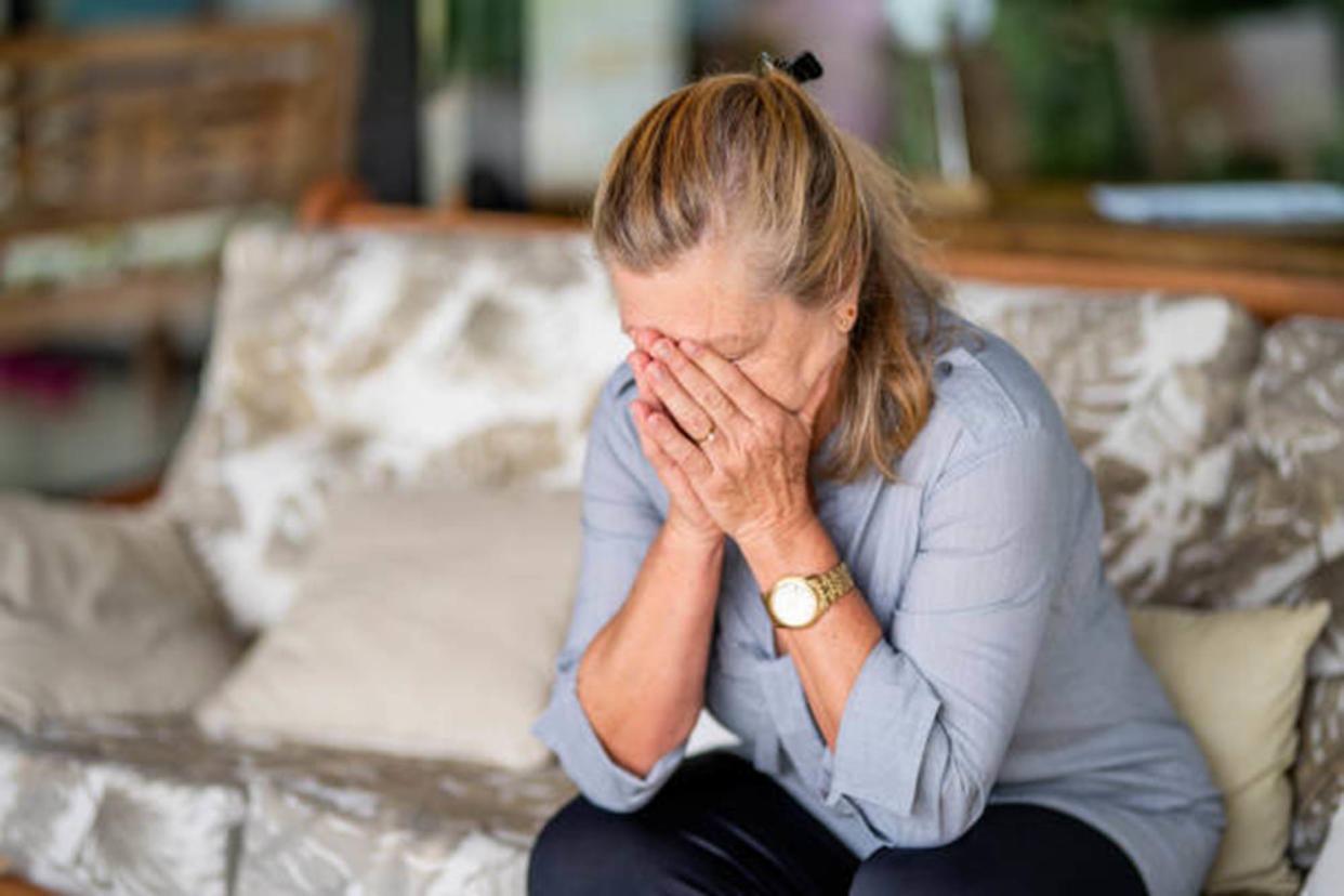 Depressed senior woman sitting alone with her head in her hands on a living room sofa at home