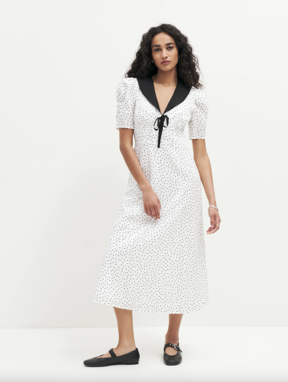 brunette model wearing black ballet flat and white dress with black polka dots, Edna Dress (Photo via Reformation)