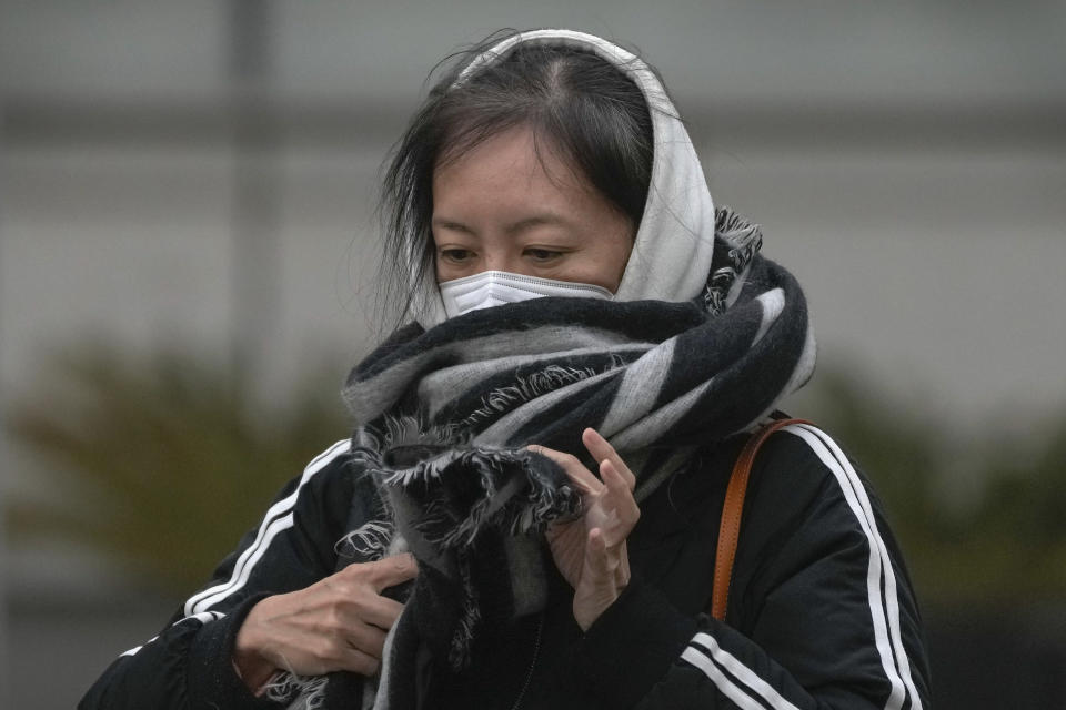 A woman wearing a face mask adjusts her scarf on a street as capital city is hit by sandstorm in Beijing, Monday, Dec. 12, 2022. China will drop a travel tracing requirement as part of an uncertain exit from its strict "zero-COVID" policies that have elicited widespread dissatisfaction. (AP Photo/Andy Wong)