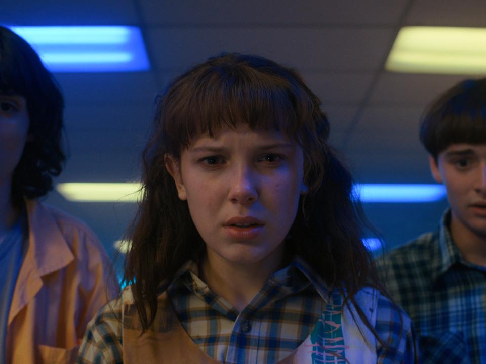 mike, eleven, and will in "Stranger Things 4," looking down at something with shocked expressions on their faces