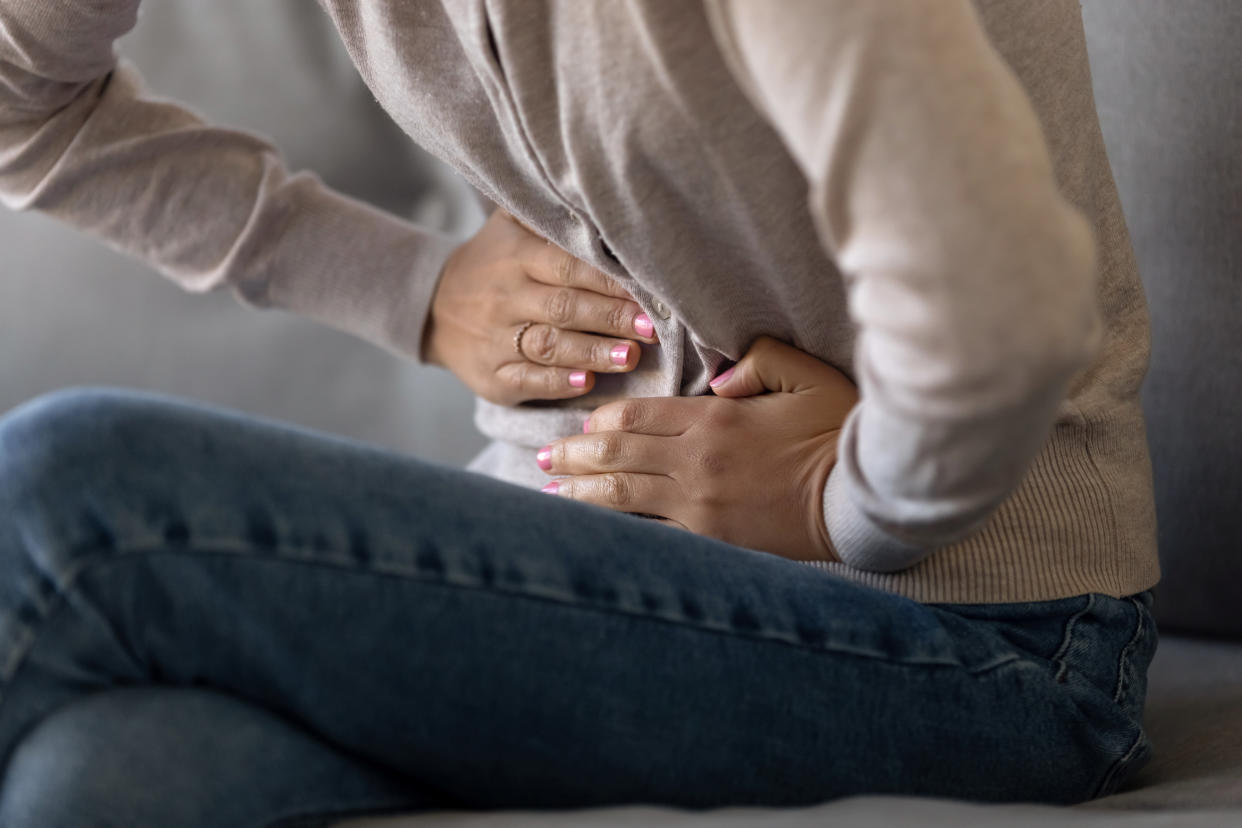 Cropped close up view girl touch stomach suffers from severe ache sitting on sofa, twinges of pain caused by menstrual period, gastric ulcer, appendicitis or disease of gastrointestinal system concept