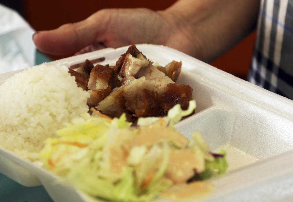 In this Thursday, March 14, 2019 photo, Belinda Lau, manager of the Wiki Wiki Drive Inn takeout restaurant in Honolulu, holds a polystyrene foam box containing an order of roast pork, rice and salad. Hawaii would be the first state in the nation to ban most plastics used at restaurants, including polystyrene foam containers, if legislation lawmakers are considering is enacted. The aim is to cut down on waste that pollutes the ocean. (AP Photo/Audrey McAvoy)