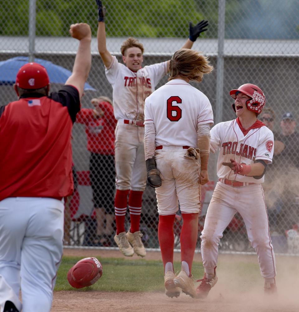 Aston Elmer of Monroe his greeted by his teammate Kellen Roberts and others after scoring the winning run in the bottom of the seventh inning as Monroe beat Bedford 2-1 in the Division 1 District Final at Ypsilanti Lincoln High School Saturday, June 4, 2022. Coach Bubba Bezeau raising his arm in victory.