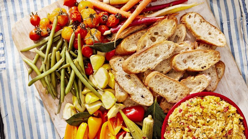 classic southern pimento cheese in a red bowl on a wooden serving board with crostini and vegetables for dipping