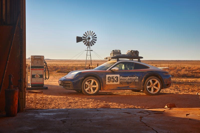 A 2023 Porsche 911 Dakar is parked in front of a windmill and a gas pump.