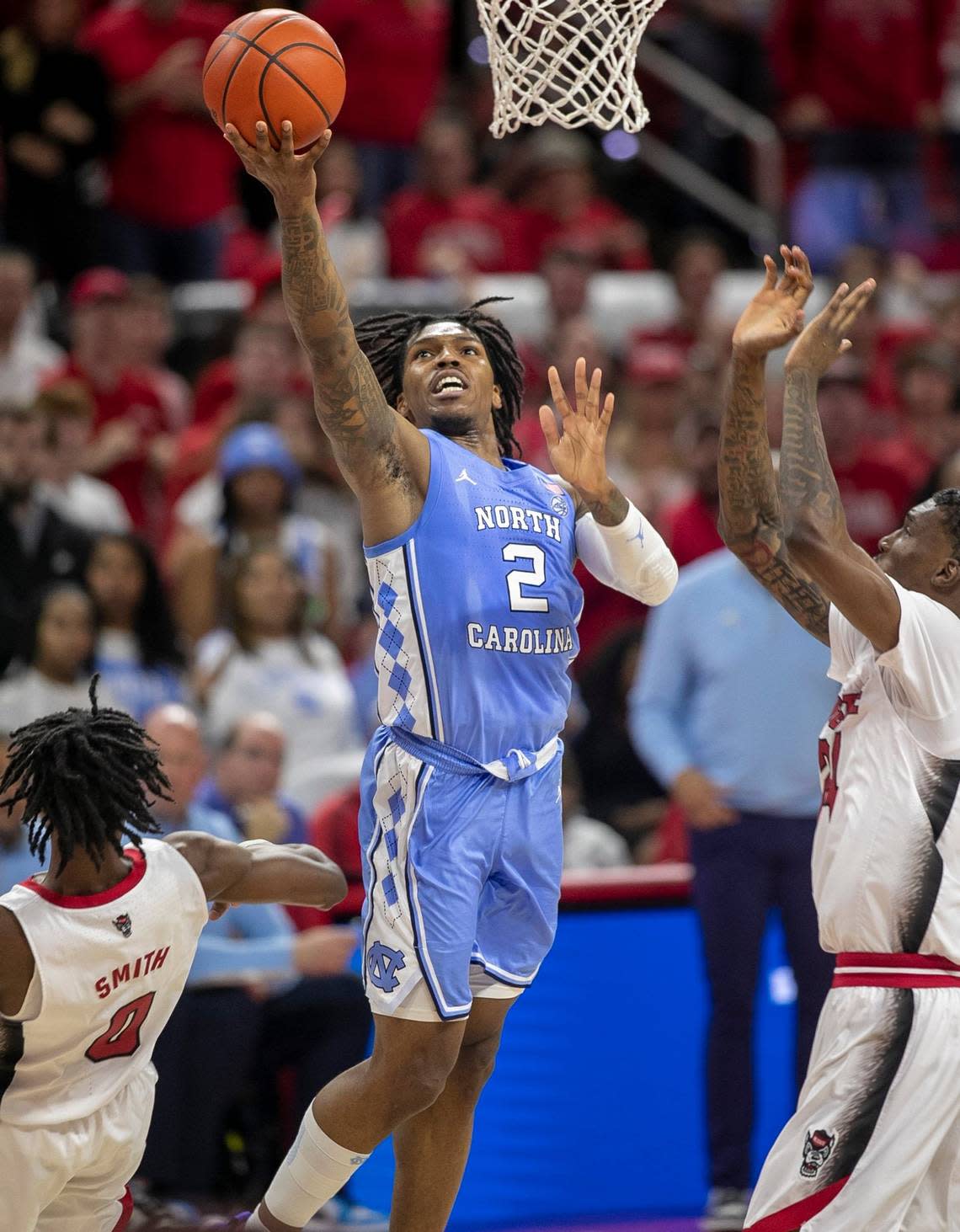 North Carolina’s Caleb Love (2) drives to the basket against N.C. State’s Terquavion Smith (0) and Ernest Ross (24) during the second half on Sunday, February 19, 2023 at PNC Arena in Raleigh, N.C. Love lead the Tar Heels with 23 points in their 77-69 loss.