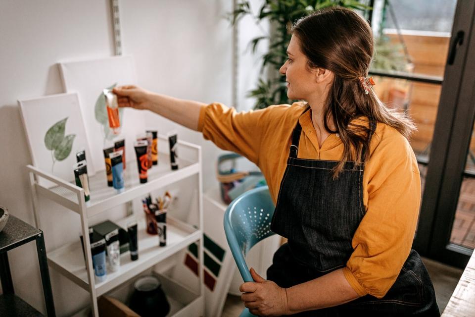 Woman in yellow blouse and black apron organizes paints on a tiered cart. 