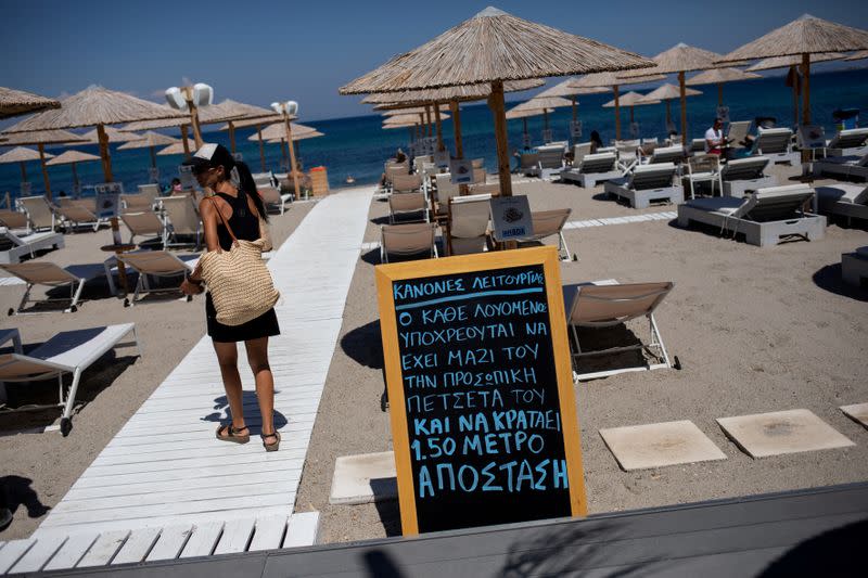 FILE PHOTO: A woman walks past an announcement calling for customers to maintain social distancing at a beach bar, following the coronavirus disease (COVID-19) outbreak, on the island of Kos