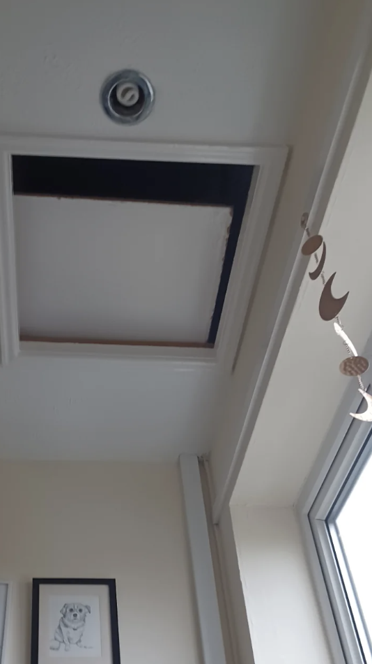 Ceiling with an open access panel and a hanging wooden moon decoration, with a framed picture on the wall