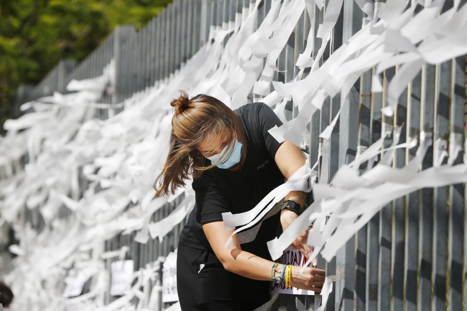 Valeria Tato, a member of Amnesty International, ties ribbons with the names of COVID-19 victims to the fence of the Public Health Ministry on World Health Day in Asuncion, Paraguay, Wednesday, April 7, 2021. (AP Photo/Jorge Saenz)