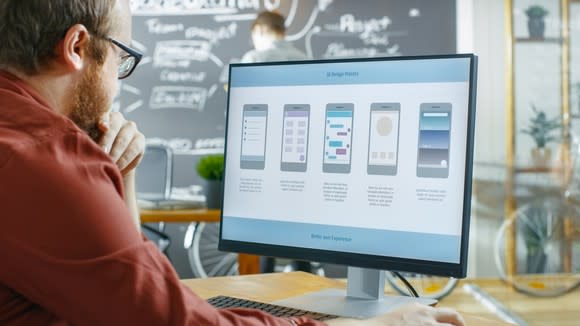 A man looking at a computer screen showing mobile app development.