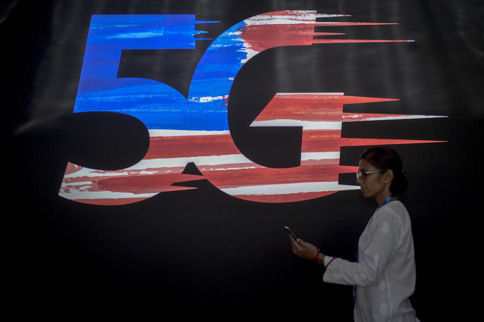 A woman uses a smartphone as she walks pass a 5G logo during the launch of the 5G Showcase in Putrajaya April 18, 2019. — Picture by Mukhriz Hazim