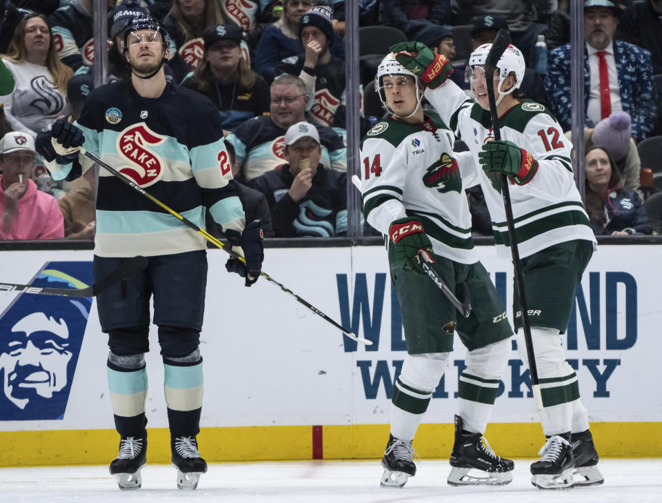 Minnesota Wild forward Matt Boldy, right, and forward Joel Eriksson Ek celebrate a goal, while Seattle Kraken defenseman Jamie Oleksiak skates past during the second period of an NHL hockey game Saturday, Feb. 24, 2024, in Seattle. (AP Photo/Stephen Brashear)