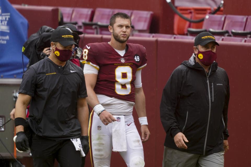 Kyle Allen walks with Washington Football Team trainers on the sideline without his helmet.