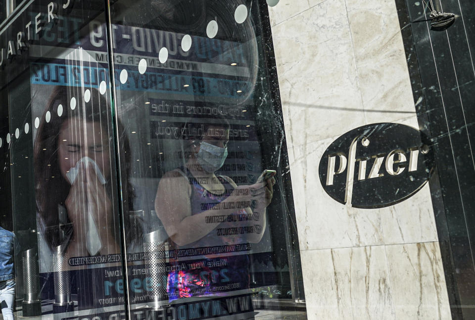 FILE - In this Nov. 9, 2020, file photo, an ad for COVID-19 testing reflects on glass at a bus stop, as pedestrians walk past Pfizer world headquarters in New York. On Friday, Nov. 20, 2020, Pfizer has asked U.S. regulators to allow emergency use of its COVID-19 vaccine, starting a process that could bring first shots as early as next month. (AP Photo/Bebeto Matthews, File)