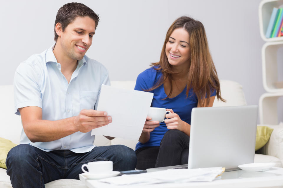 Smiling couple paying their bills online with laptop in living room at home