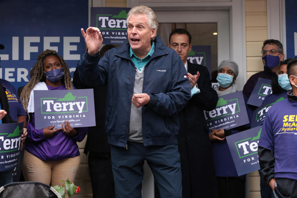 Terry McAuliffe, standing, is surrounded by supporters holding signs. 