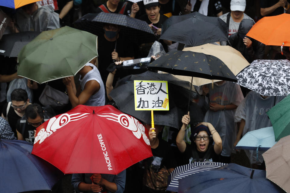 A participant reacts near a sign that reads: "Hong Kong people, Go!" during a protest rally in Hong Kong Sunday, Aug. 18, 2019. Heavy rain fell on tens of thousands of umbrella-ready protesters as they started marching from a packed park in central Hong Kong, where mass pro-democracy demonstrations have become a regular weekend activity. (AP Photo/Vincent Thian)