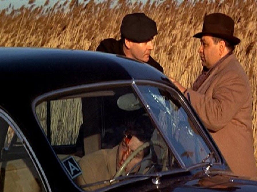 Characters Rocco and Clemenza behind a car with a man bleeding on the steering wheel.