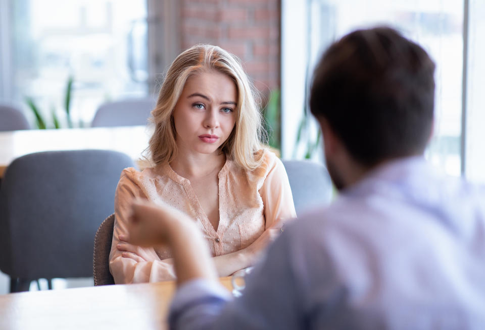 Two people are at a table having a serious conversation in a casual setting. The woman has an attentive expression