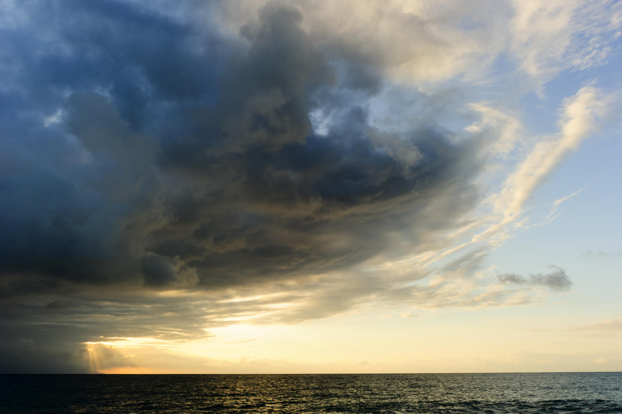 Storm clouds is an ominous storm moving in over the ocean as a bright set of sunrays burst through the darkness to light the way.