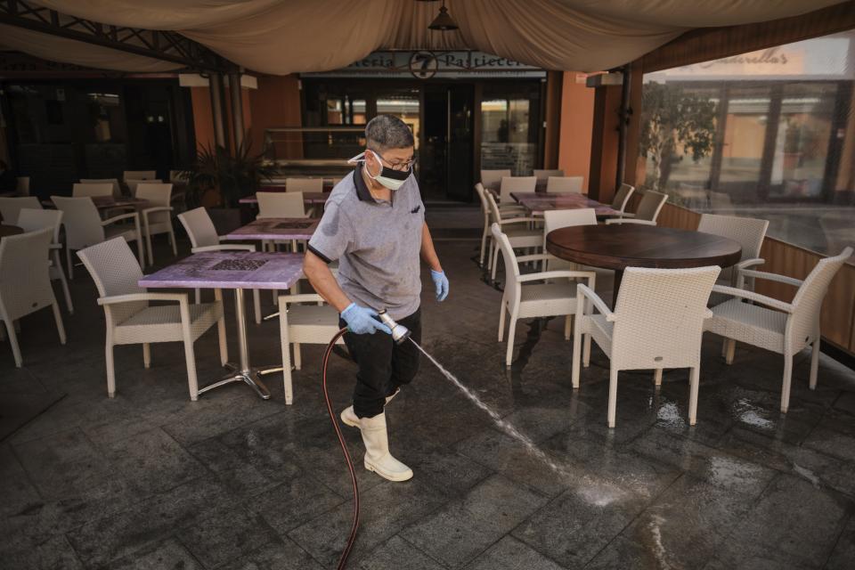 A staffer wearing a mask cleans the terrace of a shopping mall in La Caleta, in the Canary Island of Tenerife, Spain, Wednesday, Feb. 26, 2020. Worries over the ever-expanding economic fallout of the COVID-19 crisis multiplied, with factories idled, trade routes frozen and tourism crippled, while a growing list of countries braced for the illness to claim new territory. Even the Olympics, five months away, wasn't far enough off to keep people from wondering if it would go on as planned. (AP Photo)