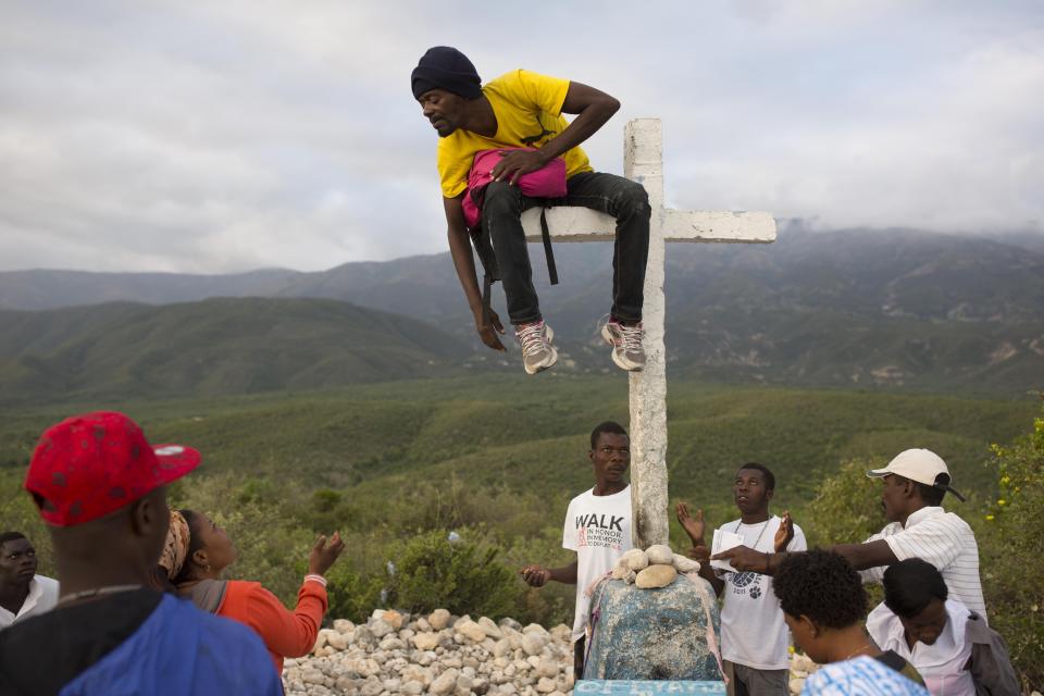 Haitians gather at the 14th station of the cross around a man sitting on the horizontal bar of the cross, who they believe has been taken over by a voodoo spirit, during the annual Good Friday pilgrimage to the mount Calvaire Miracle, in Ganthier, Haiti, Friday, April 14, 2017. (AP Photo/Dieu Nalio Chery)