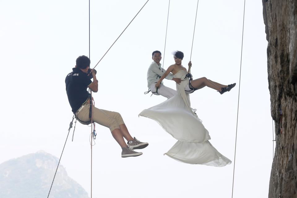 A photographer takes pictures of Fang Jing (R) in a wedding gown next to her husband, surnamed Zhao, as they hang from a cliff during a rock climbing exercise in Liuzhou, Guangxi Zhuang Autonomous Region October 26, 2013. The couple love outdoor sports and they decided to have their wedding photos taken during rock climbing, local media reported. Picture taken October 26, 2013. REUTERS/Stringer (CHINA - Tags: SOCIETY SPORT TPX IMAGES OF THE DAY) CHINA OUT. NO COMMERCIAL OR EDITORIAL SALES IN CHINA