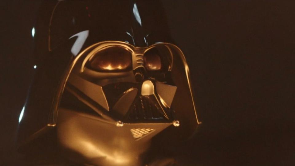 Darth Vader looking at flames in an image for the Obi-Wan Kenobi Easter Eggs and Star Wars references article. James Earl Jones returns to voice Darth Vader.