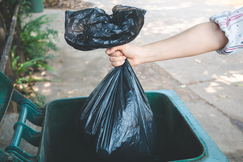 A woman throwing a bag of trash into the garbage can.