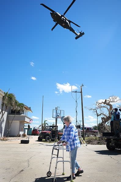 A Florida Army National Guard helicopter prepares to land as Madeline Thayer walks to an evacuation center on the island on October 2, 2022, in Pine Island, Florida. Residents are being encouraged to leave because the only road onto the island is impassable and electricity and water remain knocked out after Hurricane Ian passed through the area.