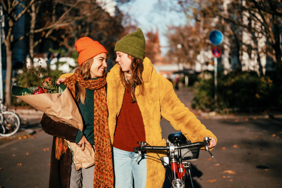 Two women smiling at each other, one with flowers and the other leaning on a bicycle