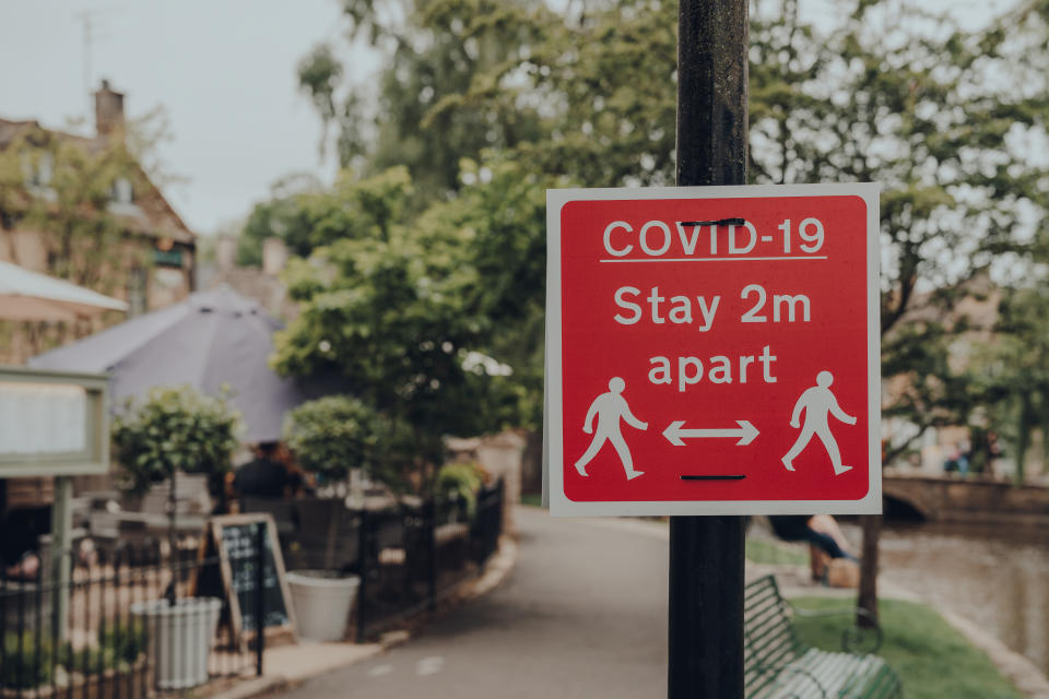 Red Covid-19 Stay 2 Metres Apart sign on a sidewalk in Bourton-on-Water, Cotswolds, UK, during COVID 19 pandemic. Selective focus.