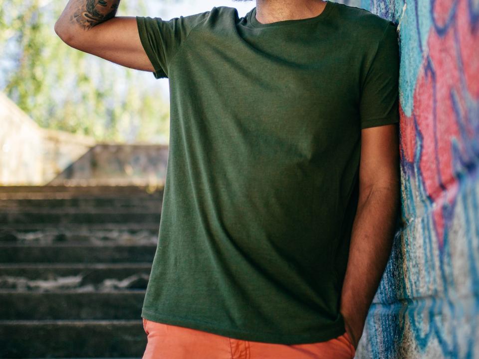 Man wearing green t-shirt and hat while leaning on wall.