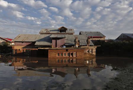 Kashmiri men stand on the roof of their flooded house as they wait to be rescued by Indian army soldiers in Srinagar September 10, 2014. REUTERS/Adnan Abidi