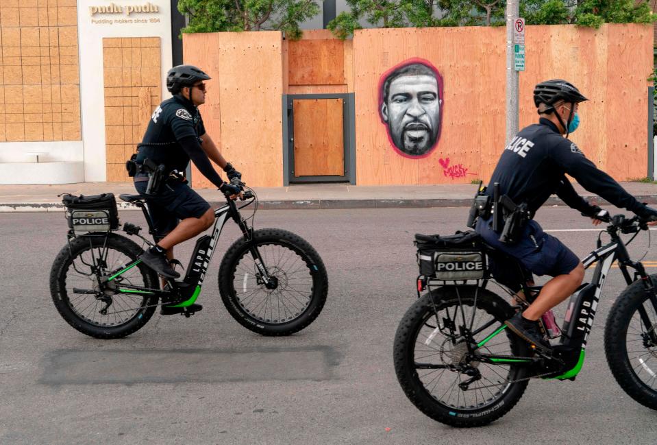 Police officers ride bicycles past a mural of George Floyd during a protest in Los Angeles in 2020.