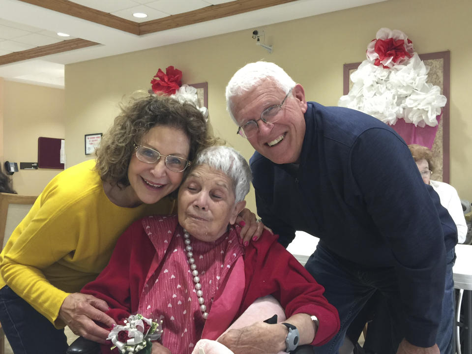 This May 2018 photo provided by Julie Griffith shows Julie Griffith, left, with her mother Mabel Porter, center, and Griffith's husband, David, as they pose for a photo at a nursing home in Oregon, Ohio. The Griffiths are among those advocating to allow cameras inside long-term care facilities. Visitation bans at nursing homes because of the coronavirus have sparked renewed interest in legislation to allow the cameras.(Julie Griffith/Julie Griffith via AP)