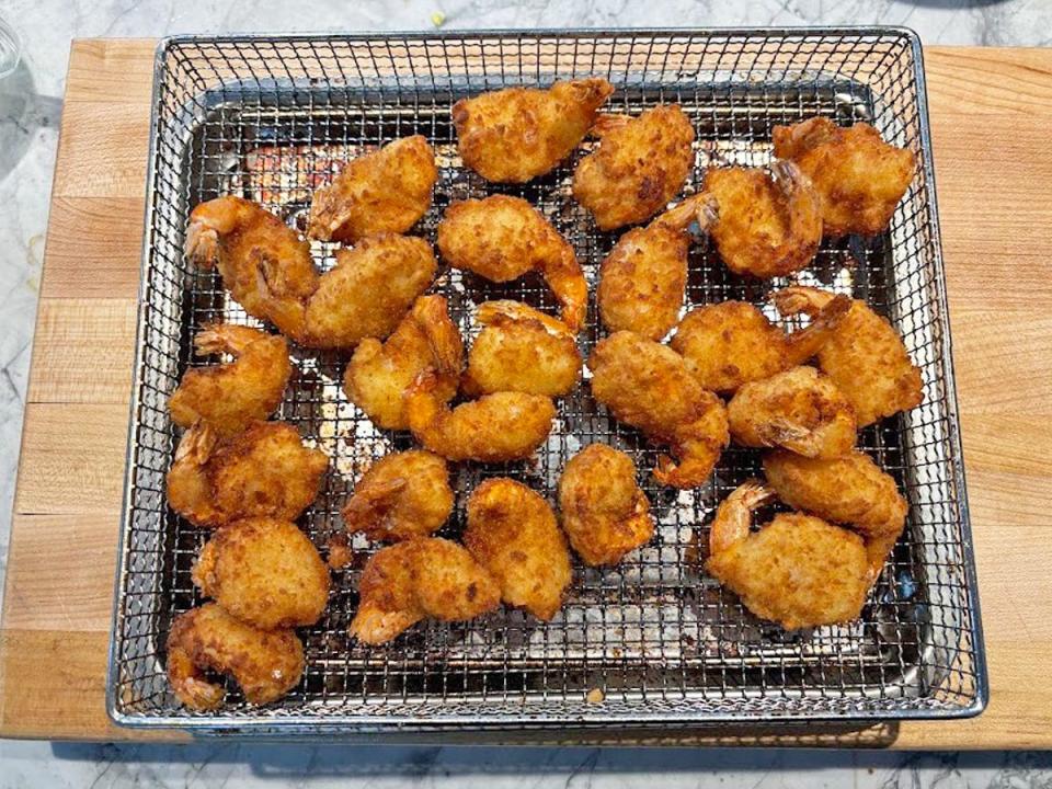 Breaded shrimp on a metal tray placed on a wooden cutting board. The shrimp is golden-brown and looks crispy