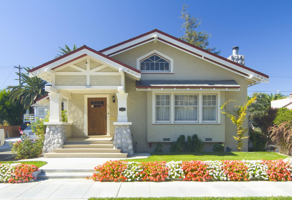 Single-story house with a charming porch and well-maintained garden in front. The house features a wooden door, stone accents, and flower beds along the walkway