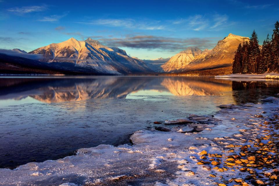 Frosty cold winter evening with sunlight over the mountains and reflections in an icy lake with snow and ice on the gravel shore