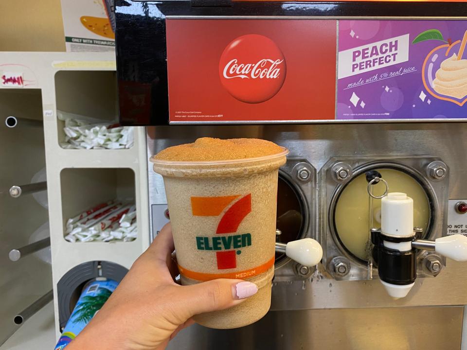 A hand filling up a large 7/11 cup with coca-cola slurpee