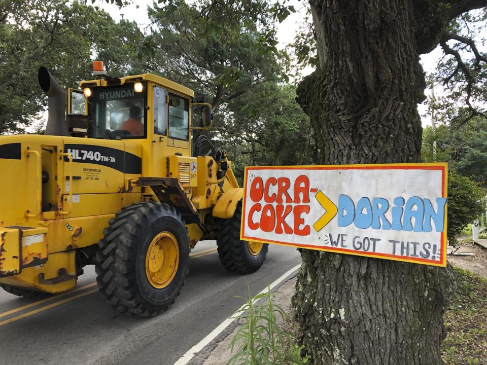 Construction equipment passes a homemade sign posted in the wake of Hurricane Dorian on North Carolina's Ocracoke Island on June 25, 2020. The secluded travel destination was ravaged by Dorian in September and then hit with coronavirus-related travel restrictions in the spring. Residents and business owners are hoping to recoup some of their losses as tourists return, albeit in smaller than usual numbers. But they're wary of a possibly busy hurricane season ahead. (AP Photo/Ben Finley).
