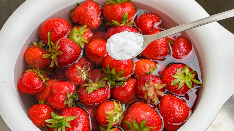 Bowl of strawberries in water with a spoon of baking soda over