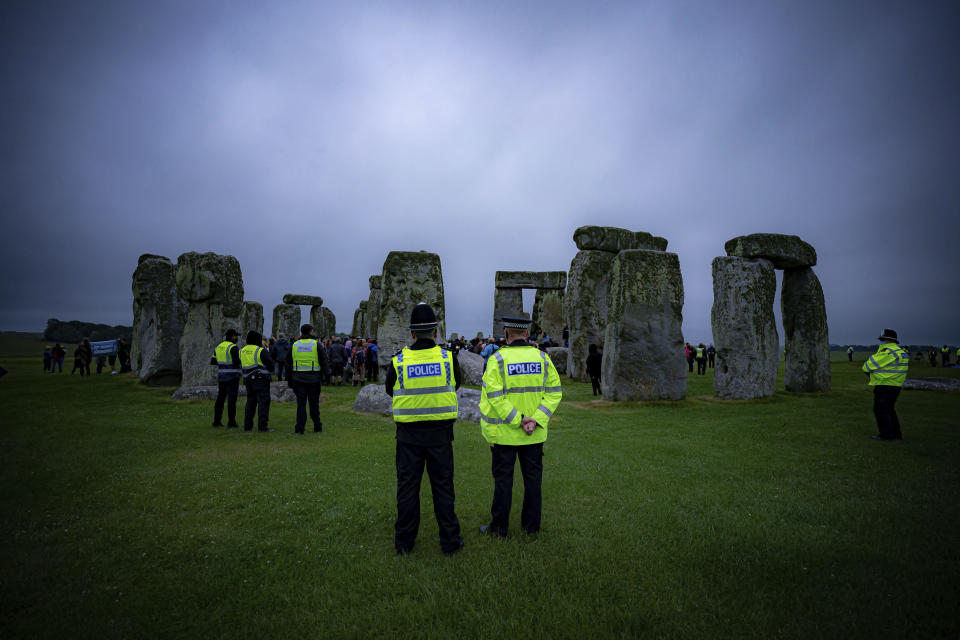 Police keep watch as people stand inside the stone circle during Summer Solstice at Stonehenge, where some people jumped over the fence to enter the stone-circle to watch the sun rise at dawn of the longest day of the year in the UK, in Amesbury, England, Monday June 21, 2021. The prehistoric monument of ancient stones have been officially closed for the celebrations due to the coronavirus lockdown, but groups of people ignored the lockdown to mark the Solstice, watched by low key security. (Ben Birchall/PA via AP)