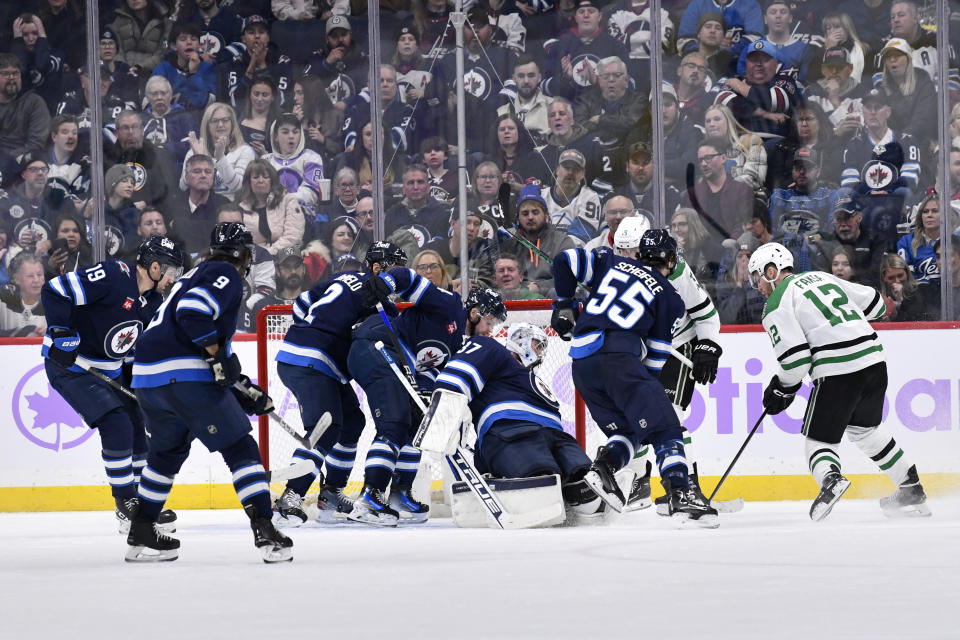 Winnipeg Jets goaltender Connor Hellebuyck (37) and his teammates look to cover up a loose puck as Dallas Stars' Radek Faksa (12) looks for the puck during the second period of an NHL hockey match in Winnipeg, Manitoba, on Tuesday, Nov. 28, 2023. (Fred Greenslade/The Canadian Press via AP)