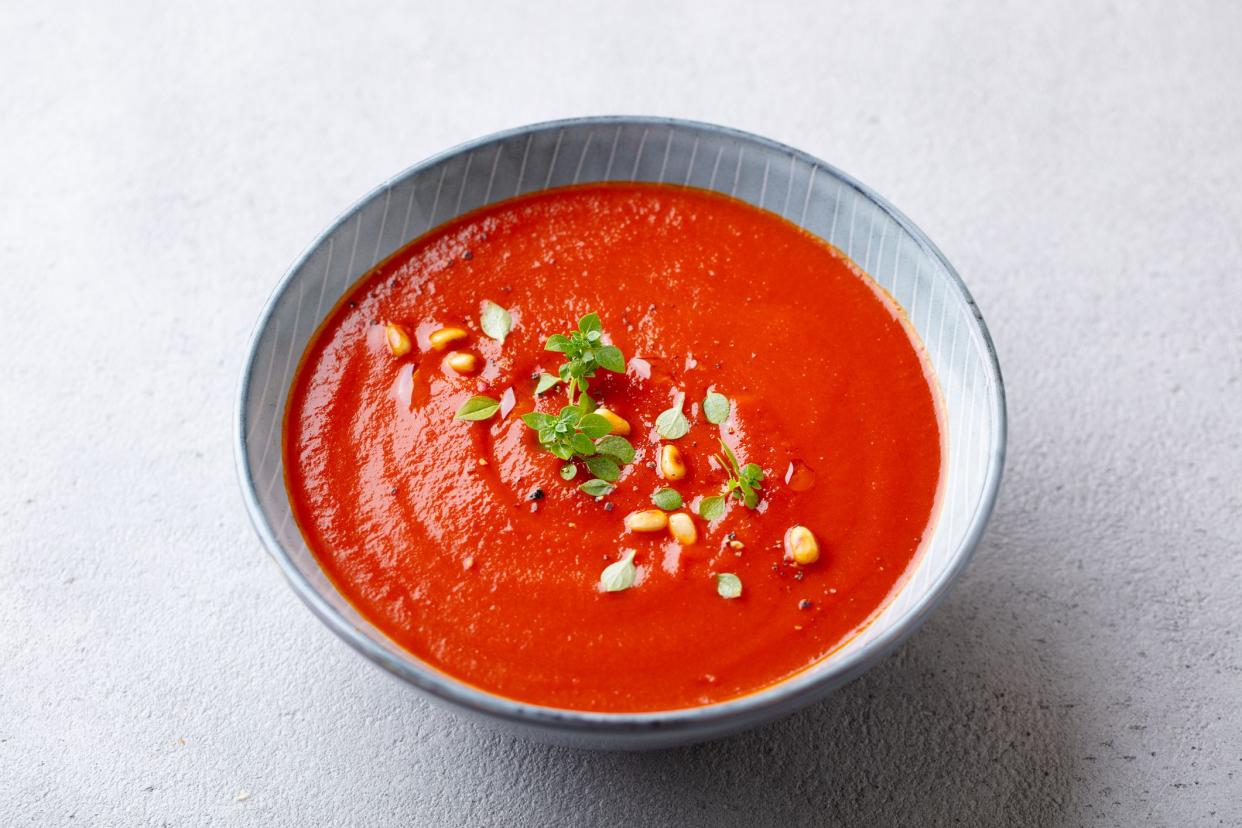 Tomato soup with fresh herbs and pine nuts in a bowl. Grey stone background. Close up.